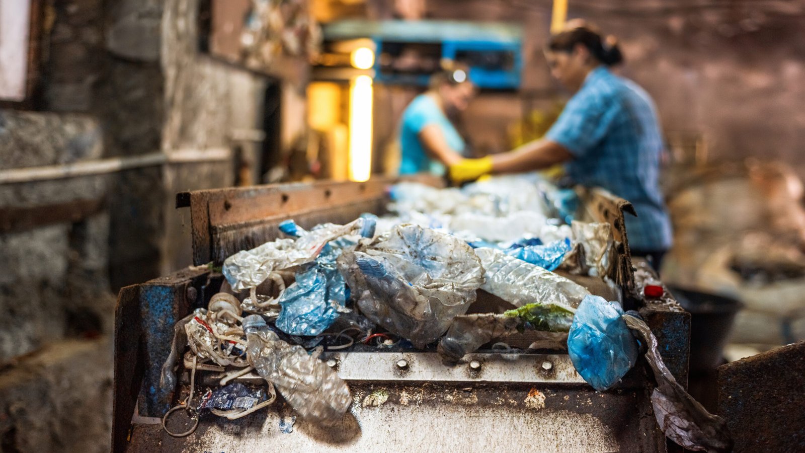 Plastic garbage on a conveyor belt at waste recycling factory. Workers on the background